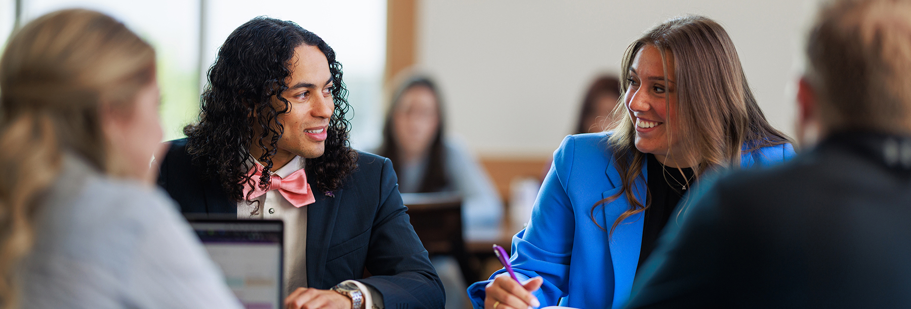 Section Image: Students at a table looking at each other 