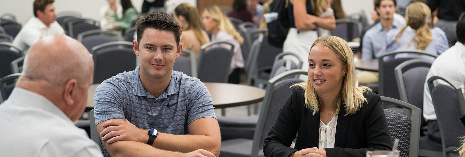 Section Image: Students and adults mingling around tables in the Hays Banquet Hall 