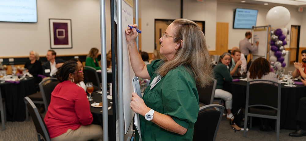 Smith Banquet Hall with people at round tables and individuals writing on a marker board