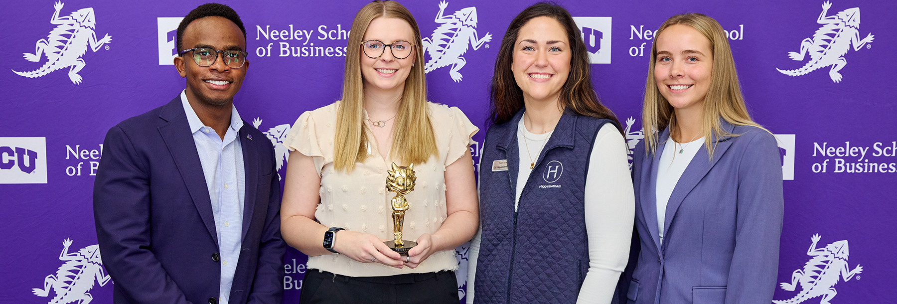 Section Image: Students posing in front of Purple Neeley background with an trophy of a gold superfrog 