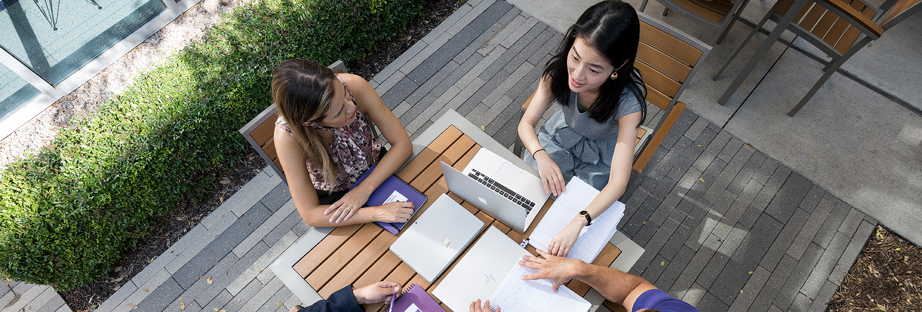 Section Image: A group sits around a table outside with laptops and notebooks. 