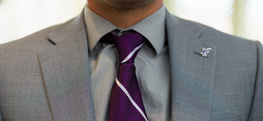 Section Image: Purple tie and horned frog lapel pin on a gray suit 