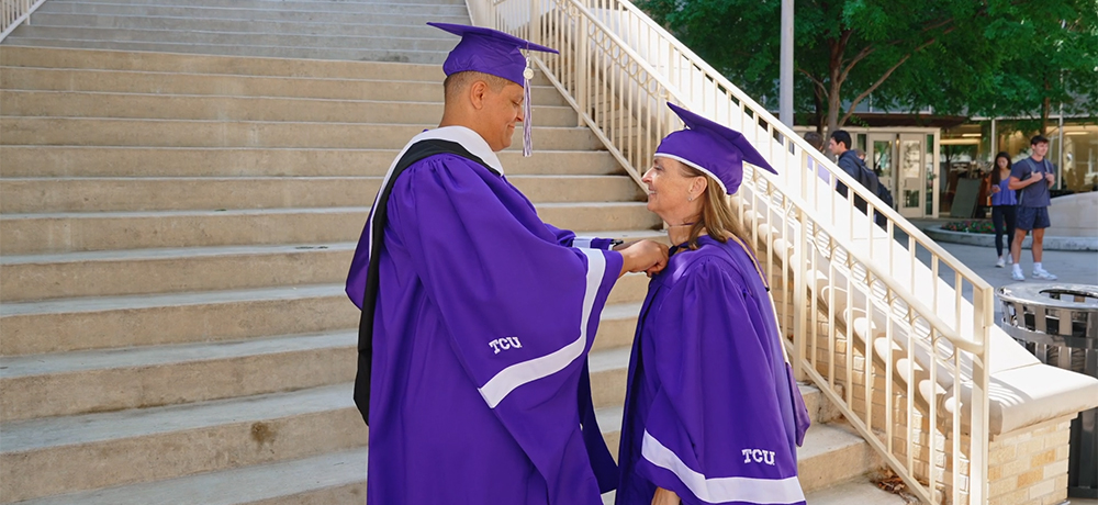 Kyle and Brandi fields in cap and gown by the Neeley steps